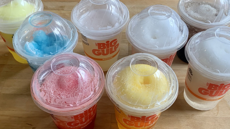 8 different slurpees in plastic cups on wooden table