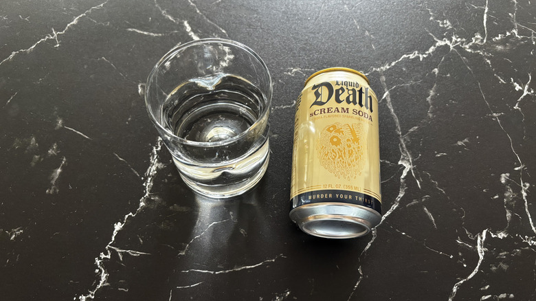 Glass of sparkling water next to sCream Soda Liquid Death soda can