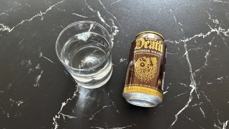 Glass of sparkling water next to Liquid Death root beer soda can