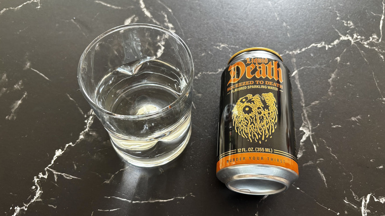 Glass of sparkling water next to Liquid Death Squeezed to Death soda can
