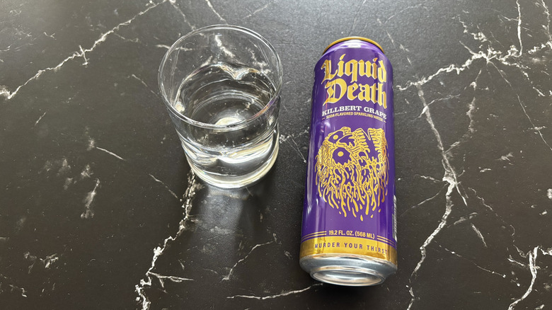 Glass of sparkling water next to Liquid Death Killbert Grape soda can