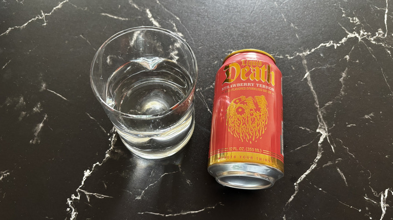 Glass of sparkling water next to Liquid Death Strawberry Terror soda can