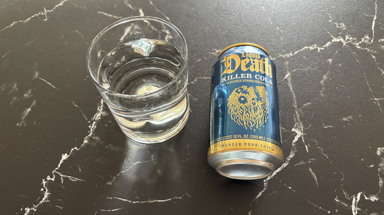 Glass of sparkling water next to Liquid Death Killer Cola soda can