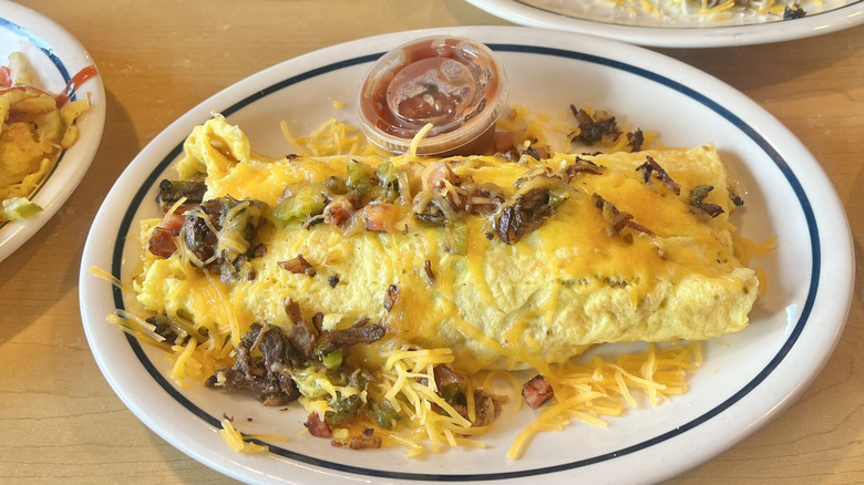 View of the Colorado Omelette on a white oval plate with sauce served on the side in a plastic container