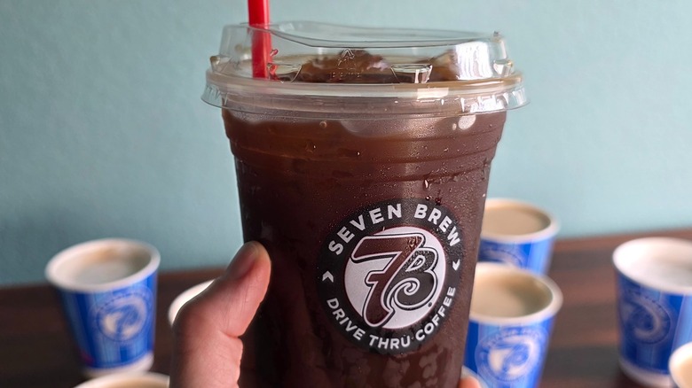 Hand holding cold brew coffee with hot coffee drinks in background