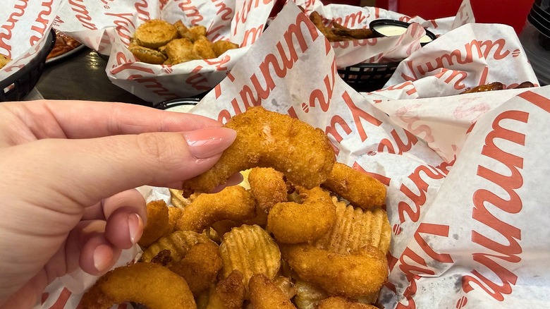Hand holding fried shrimp above basket of shrimp and chips at Red Robin
