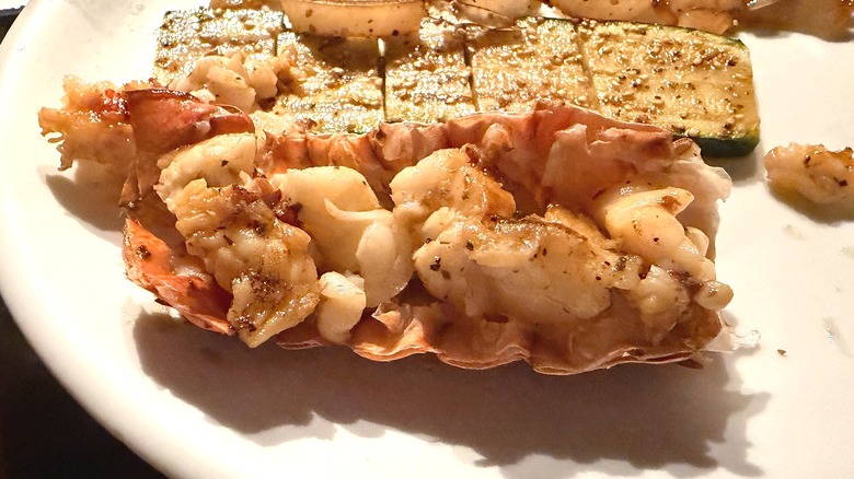 Close-up of Benihana cold-water lobster tail on white plate, zucchini behind