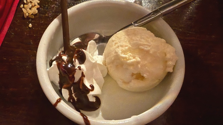 Close-up of vanilla ice cream and whipped cream with chocolate drizzle in bowl on table at restaurant
