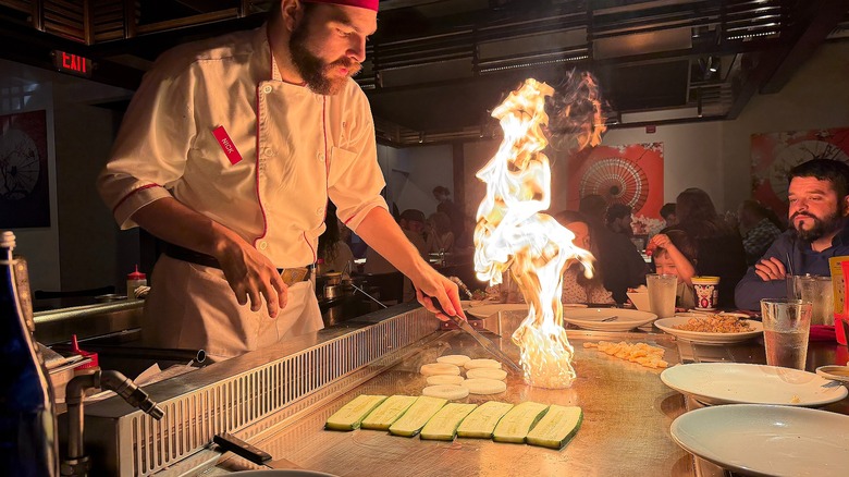 Benihana chef cooking onion and zucchini, flame rising up from flat top