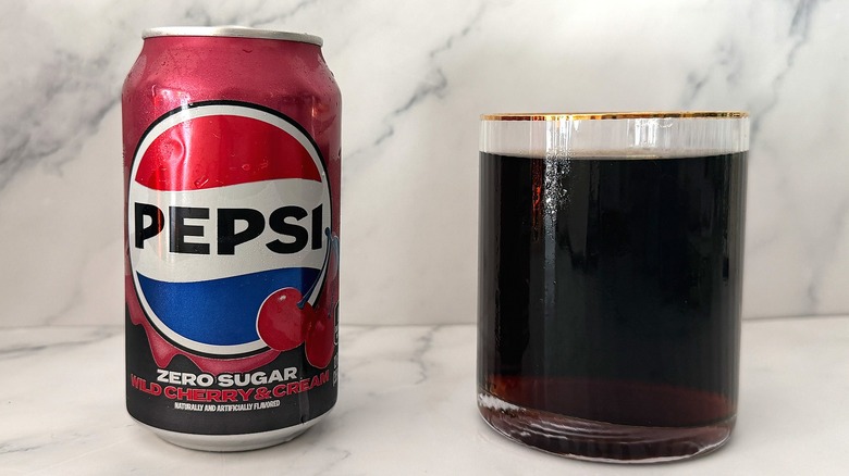 Can of Zero Sugar Wild Cherry & Cream Pepsi next to gold-rimmed glass of Pepsi on marble surface