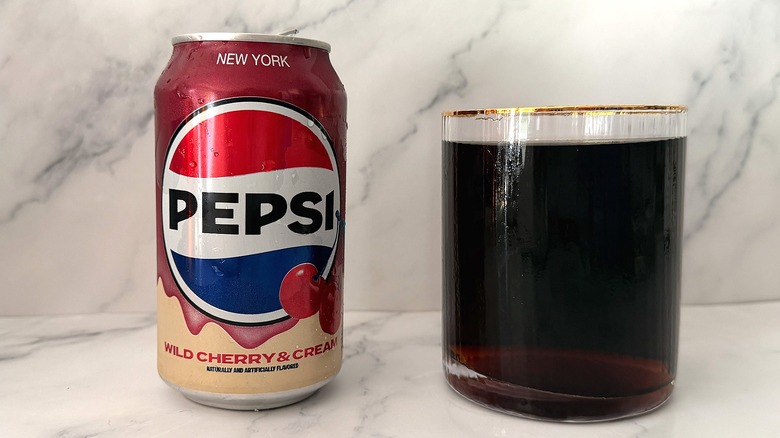Can of Wild Cherry & Cream Pepsi next to gold-rimmed glass of Pepsi on marble surface