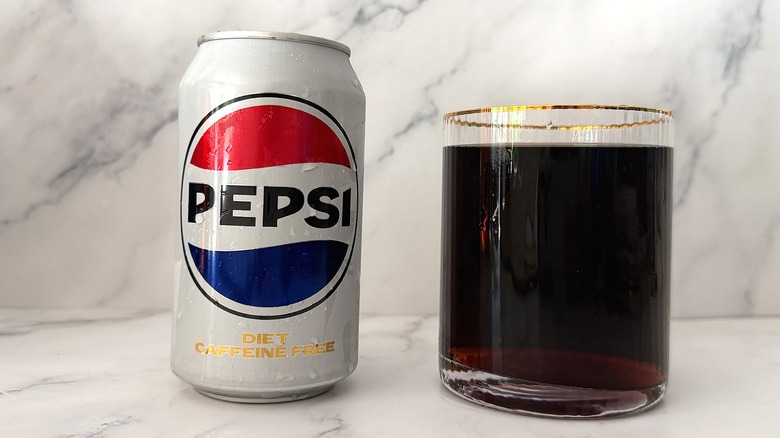 Can of Diet Caffeine Free Pepsi next to gold-rimmed glass of Pepsi on marble surface