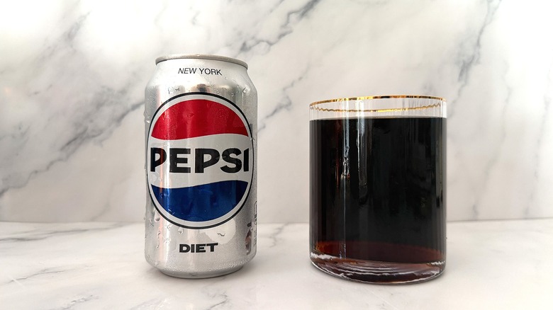 Can of Diet Pepsi next to gold-rimmed glass of Pepsi on marble surface