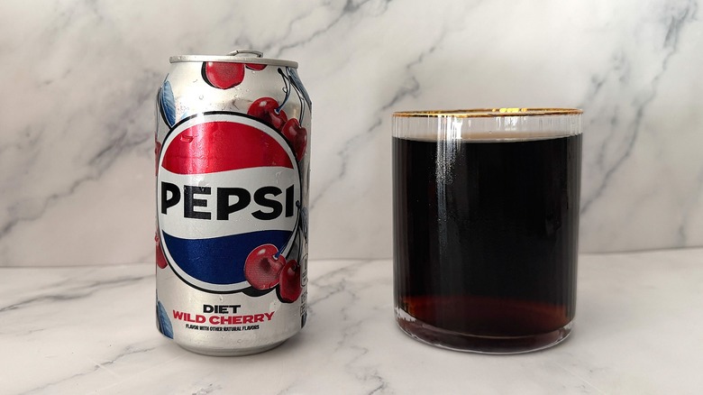 Can of Diet Wild Cherry Pepsi next to gold-rimmed glass of Pepsi on marble surface