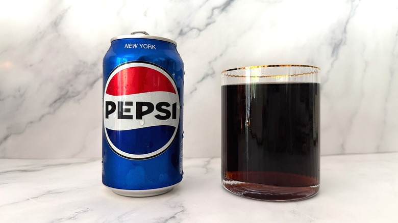 Can of Pepsi next to gold-rimmed glass of Pepsi on marble surface
