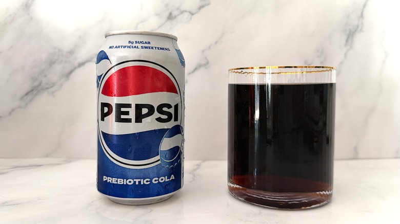Can of Pepsi Prebiotic Cola next to gold-rimmed glass of Pepsi on marble surface