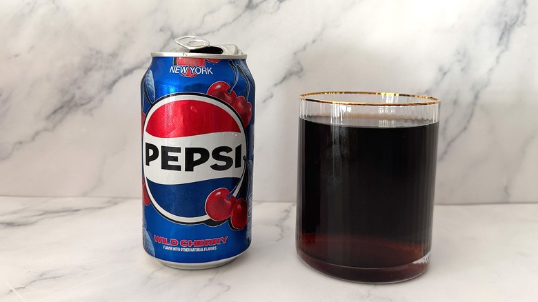 Can of Wild Cherry Pepsi next to gold-rimmed glass of Pepsi on marble surface