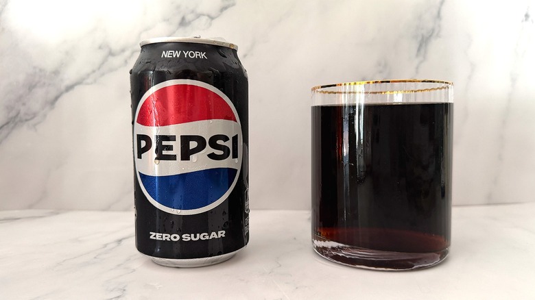 Can of Zero Sugar Pepsi next to gold-rimmed glass of Pepsi on marble surface