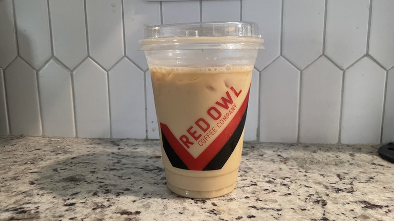 Cup of Red Owl iced latte on countertop with white tiles in the background