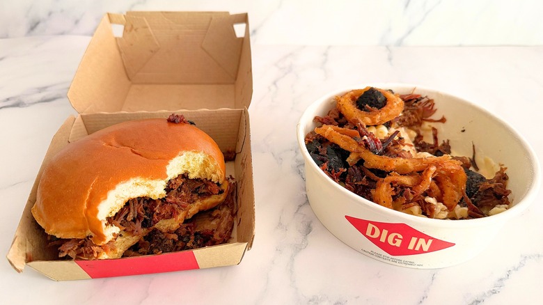 Half-eaten Arby's brisket sandwich and mac bowl on marble surface