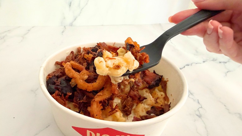 Hand holding fork of food above Arby's Mac Bowl on marble surface