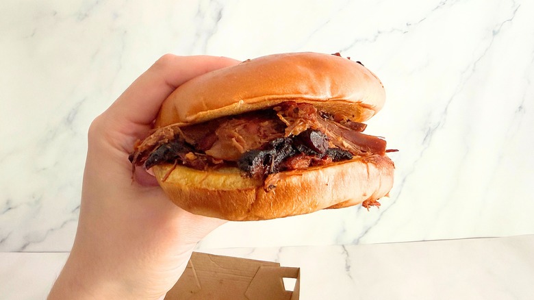 Hand holding Arby's chopped brisket sandwich against marble background