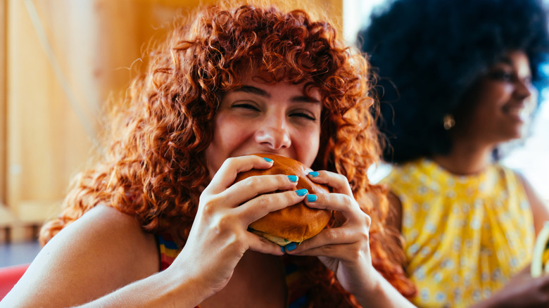 A happy woman in a restaurant taking a bite of a burger