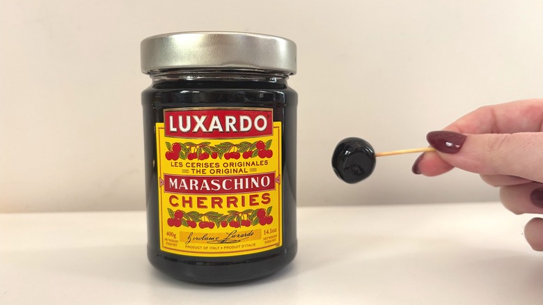 Jar of Luxardo Maraschino cherries next to hand holding cherry on toothpick