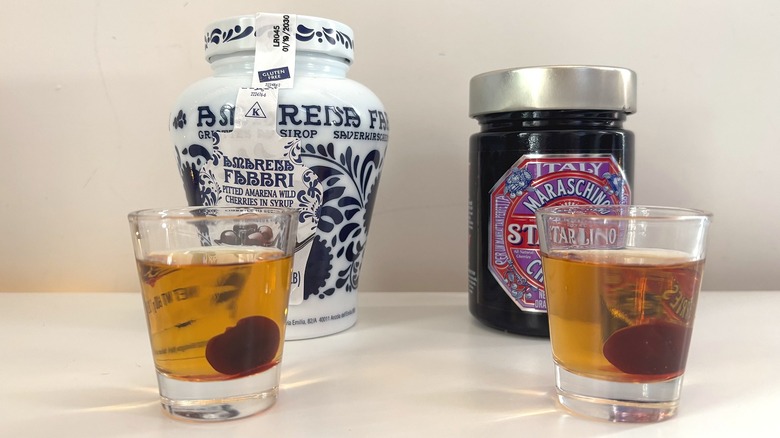 Jars of Fabbri and Hotel Starlino cocktail cherries behind shot glasses with whiskey and cocktail cherries