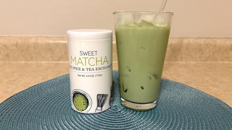The Spice & Tea Exchange sweet matcha in tin and glass on a blue placemat and neutral background