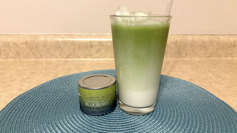 The Spice & Tea Exchange blueberry matcha in tin and glass on a blue placemat and neutral background