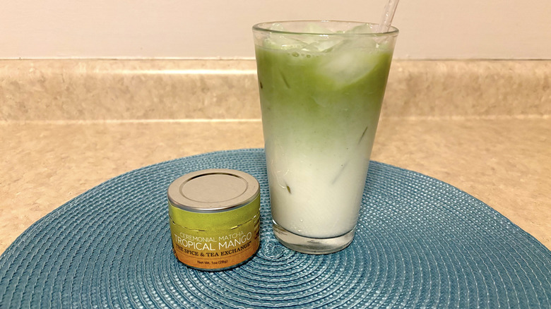 The Spice & Tea Exchange tropical mango matcha in tin and glass on a blue placemat and neutral background