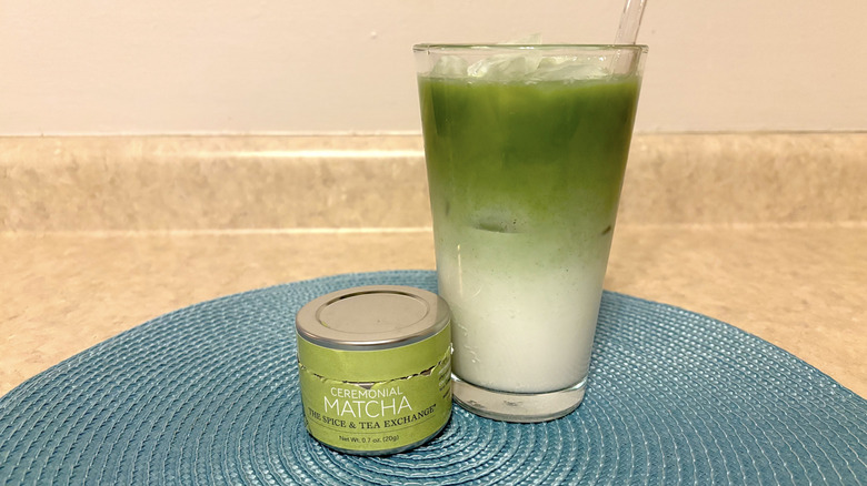 The Spice & Tea Exchange ceremonial matcha in tin and glass on a blue placemat and neutral background