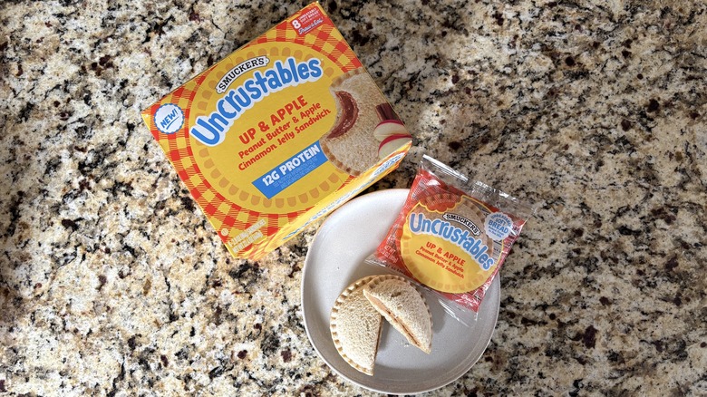 Up & apple Uncrustables in box, package, and on plate on marble countertop
