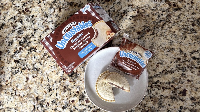 Chocolate flavored hazelnut spread Uncrustables Uncrustables in box, package, and on plate on marble countertop