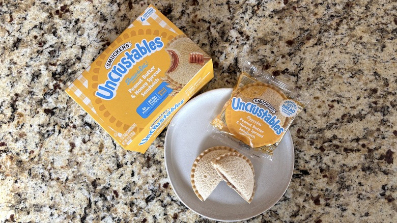 Peanut butter and honey spread Uncrustables Uncrustables in box, package, and on plate on marble countertop