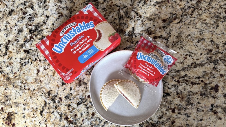 Peanut butter and strawberry jam Uncrustables in box, package, and on plate on marble countertop