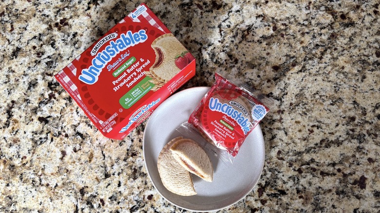 Peanut butter and strawberry reduced sugar Uncrustables in box, package, and on plate on marble countertop