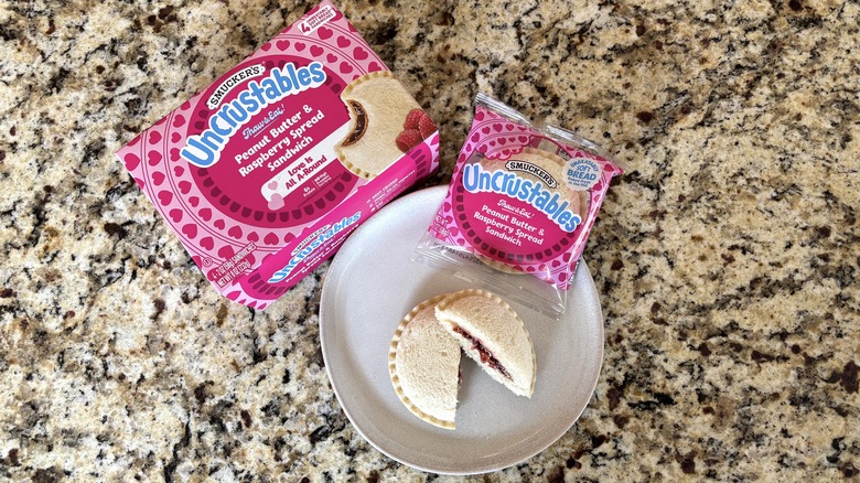 Peanut butter and raspberry spread Uncrustables in box, package, and on plate on marble countertop