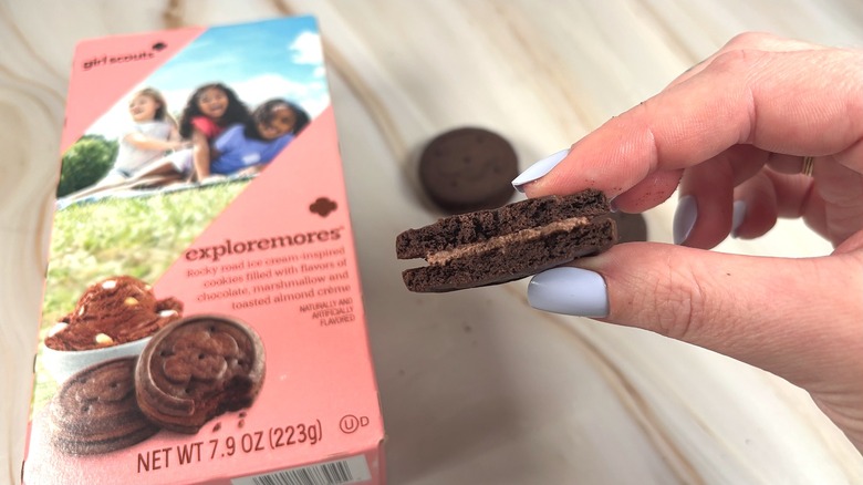 Hand holding Exploremores cookie with bite taken out of it, box behind
