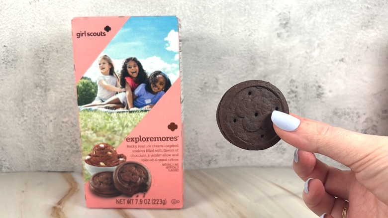 Hand holding Exploremores cookie, pink cookie box behind