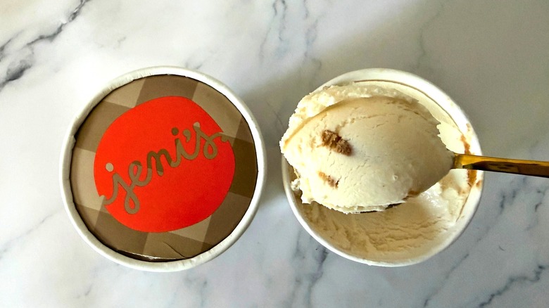 Top-down shot of Jeni's Appalachian Acorn Pie ice cream pints, spoon holding scoop of ice cream over one, all on marble surface