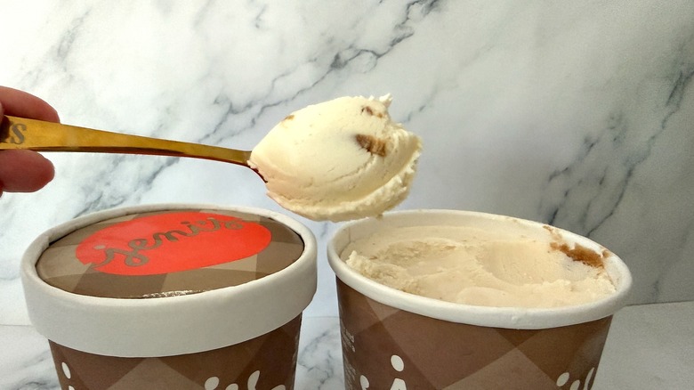 Hand holding spoonful of ice cream over two pints of ice cream on marble background
