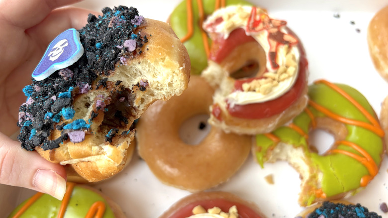 A hand holding the Skeletor Double Chocolate Doughnut with a bite taken out of it