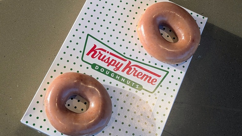 Two Apple Cider Original Glazed donuts resting on top of a small Krispy Kreme box