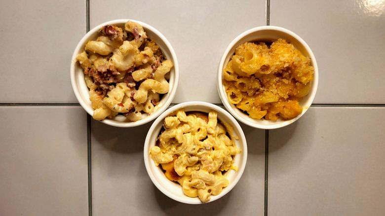 Three ramekins of macaroni and cheese sit on a white tile table.
