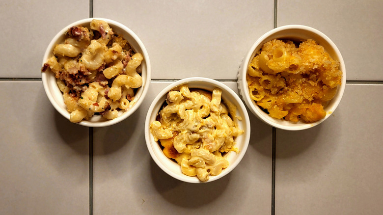 Three ramekins filled with mac and cheese on a white tile table.