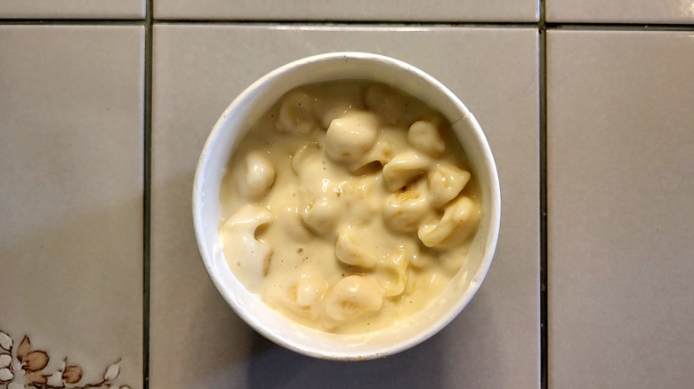 A white ramekin filled with a creamy macaroni and cheese sitting on a white tile table.