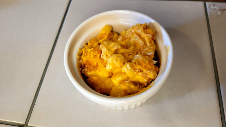 A white ramekin full of pasta with a yellow sauce and breadcrumbs on a white tile table.