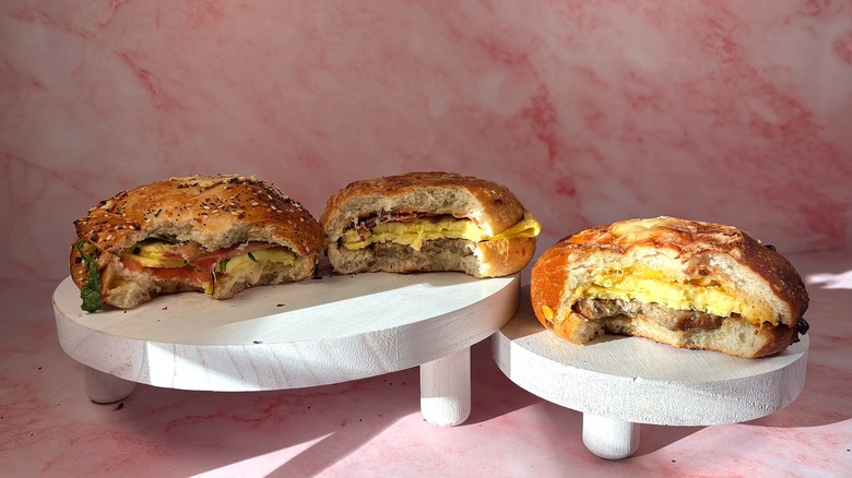 Three Panera Asiago Bagel Stacks with bites taken out on white platforms, pink marble background